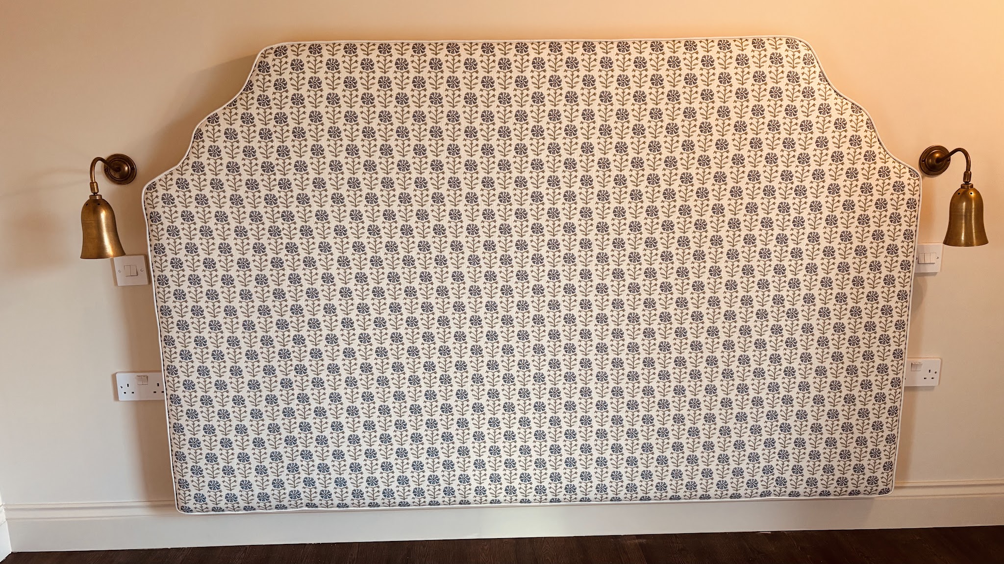 Shaped upholstered headboard fitted to the wall between two wall lights