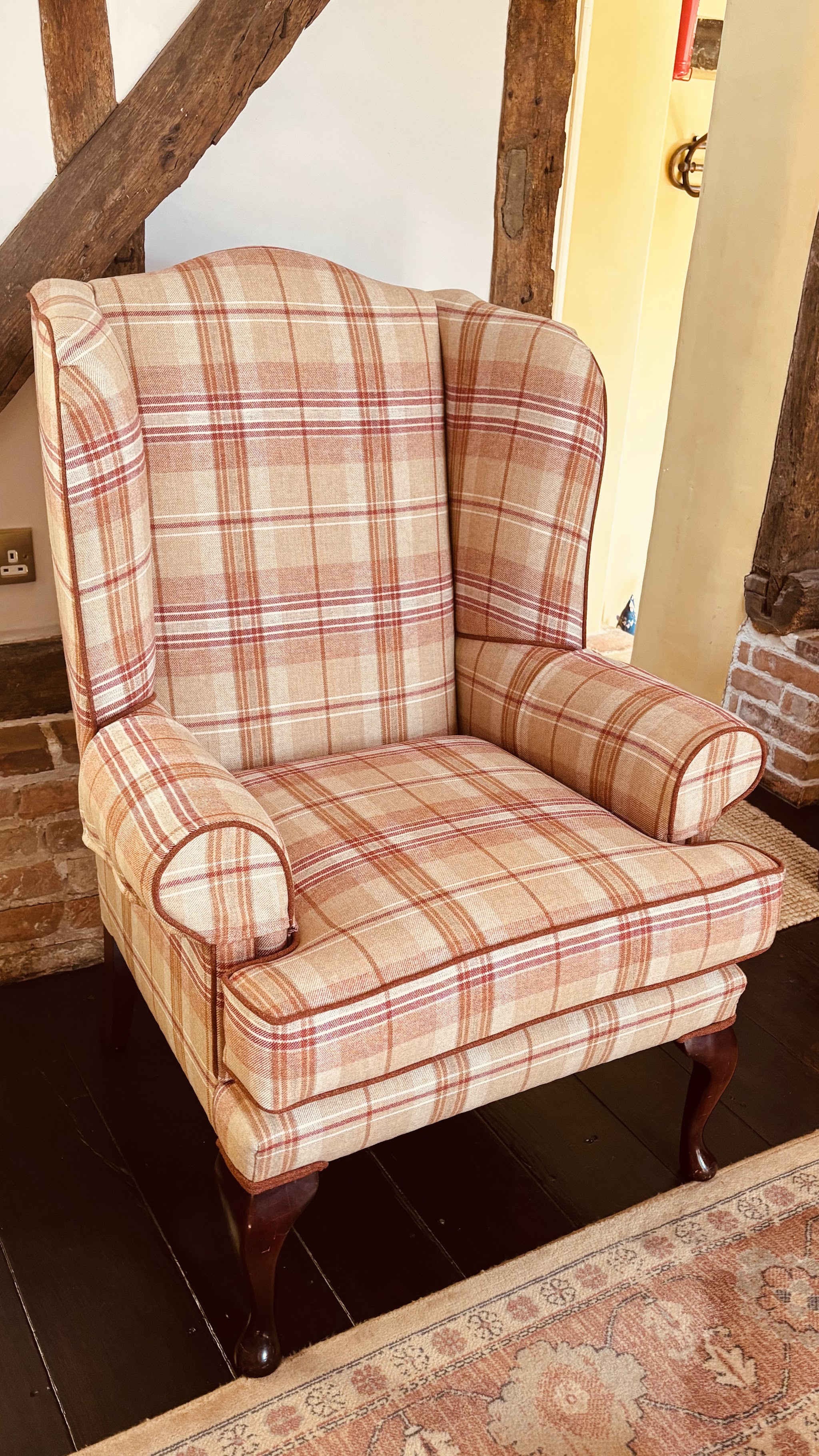 Wing chair in a red and cream check under oak beams