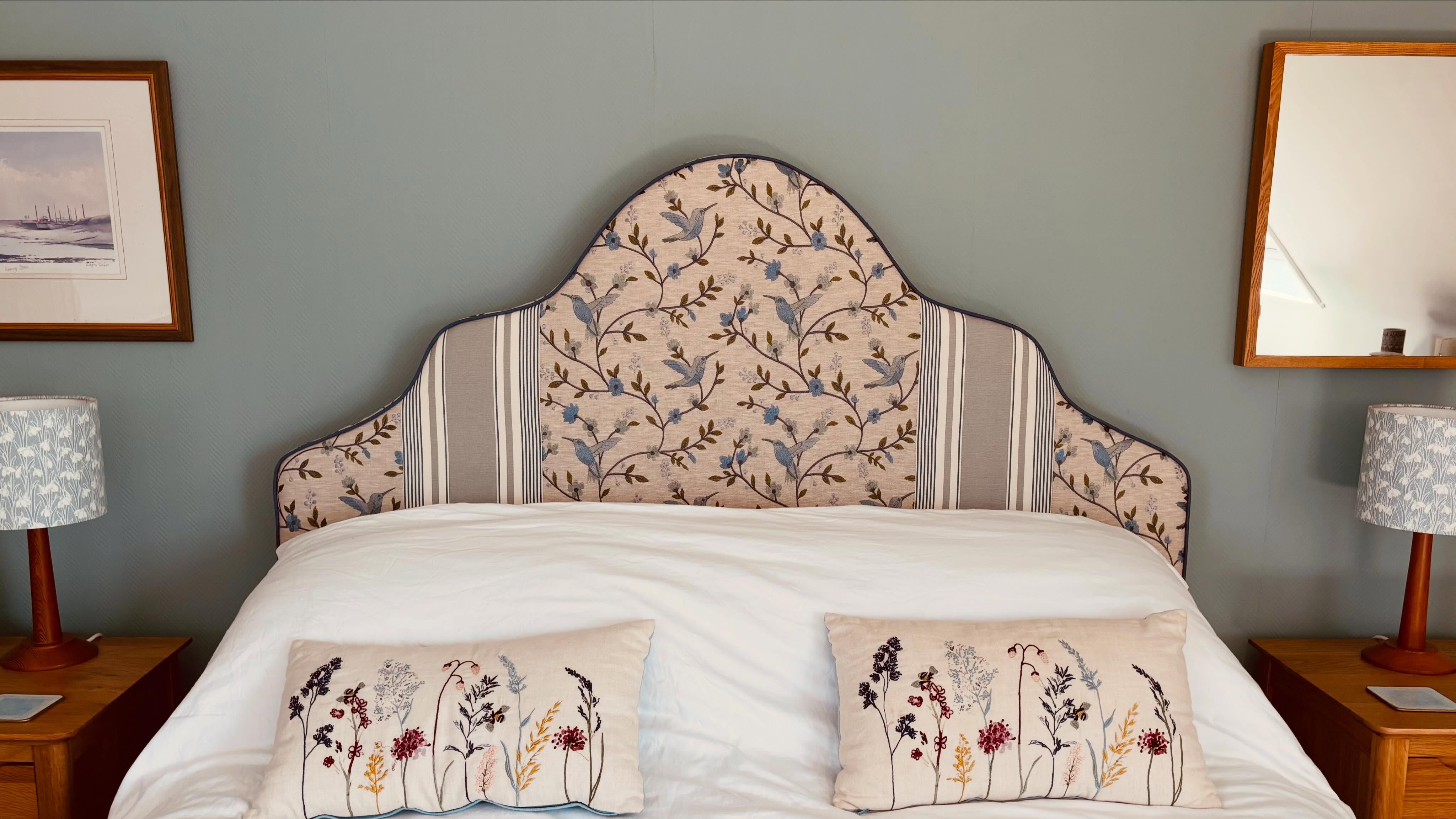 A bespoke kingsize headboard in embroidered bird fabric with striped borders, behind a made bed with matching cushions